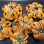 Halloween-Kürbisbrötchen mit grünem Garn auf einer dunklen Schieferplatte.