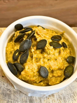 Kürbis-Pesto in einer weißen Schale angerichtet und mit Kürbiskernen dekoriert.