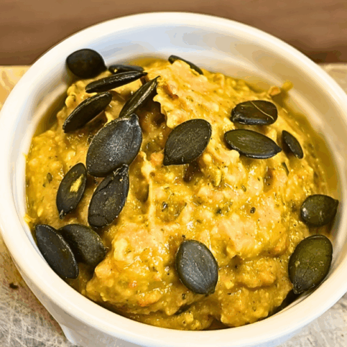 Kürbis-Pesto in einer weißen Schale angerichtet und mit Kürbiskernen dekoriert.