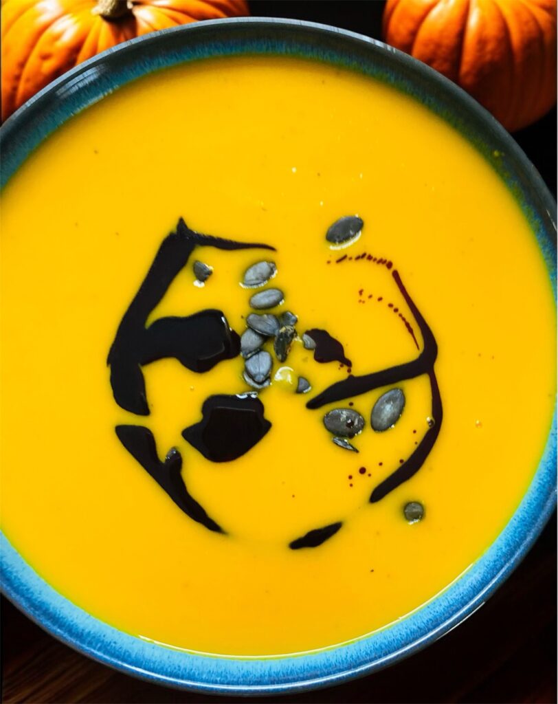 Kürbiscremesuppe in einer blauen Schale mit Kürbiskernöl und Kürbiskernen dekoriert. Im Hintergrund Kürbisse