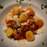 Gnocchi-Gröstl mit würziger Salsiccia und Herbstgemüse auf einem Teller mit Parmesan-Streifen serviert