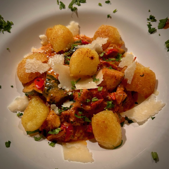 Gnocchi-Gröstl mit würziger Salsiccia und Herbstgemüse auf einem Teller mit Parmesan-Streifen serviert