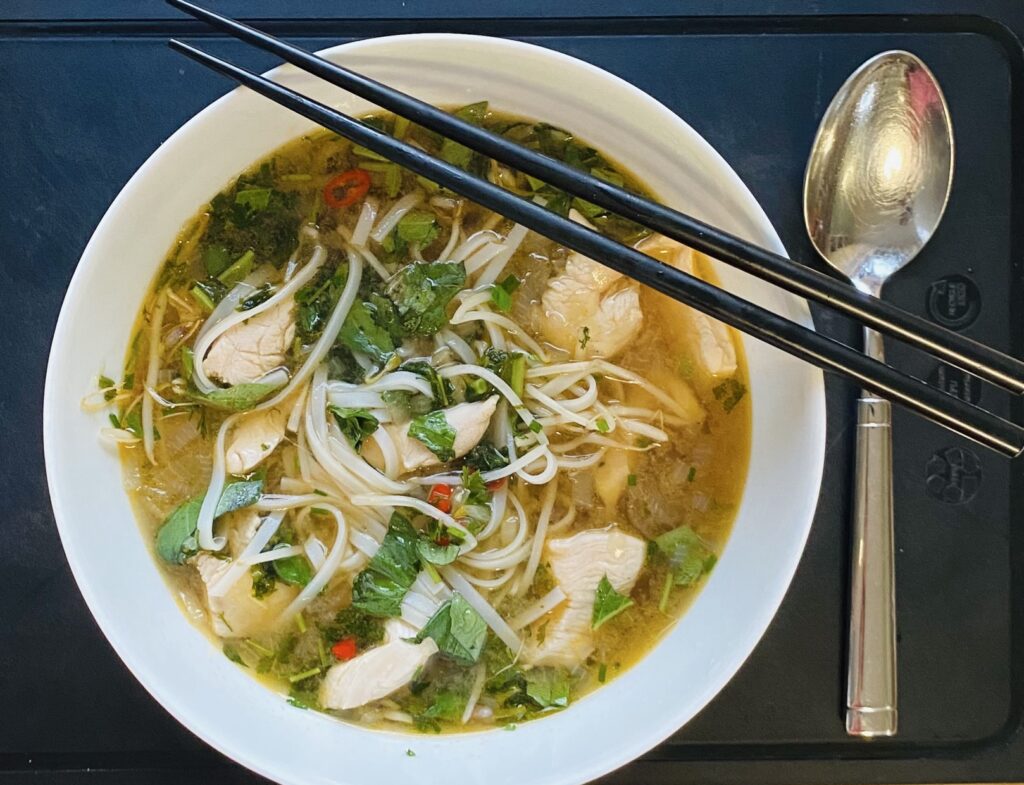 Pho Ga Suppe mit Huhn & Reisnudeln in einer Schale serviert. Wer mag kann die Reisnudeln gerne mit Stäbchen essen, so richtig traditionell.
