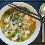 Pho Ga Suppe mit Huhn & Reisnudeln in einer Schale serviert. Wer mag kann die Reisnudeln gerne mit Stäbchen essen, so richtig traditionell.