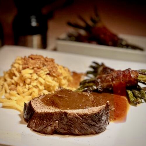 Geschmorte Lammkeule mit Spätzle und gerösteten Semmelbösel mit einer kräftigen dunklen Soße und Bohnen in Speck angerichtet.