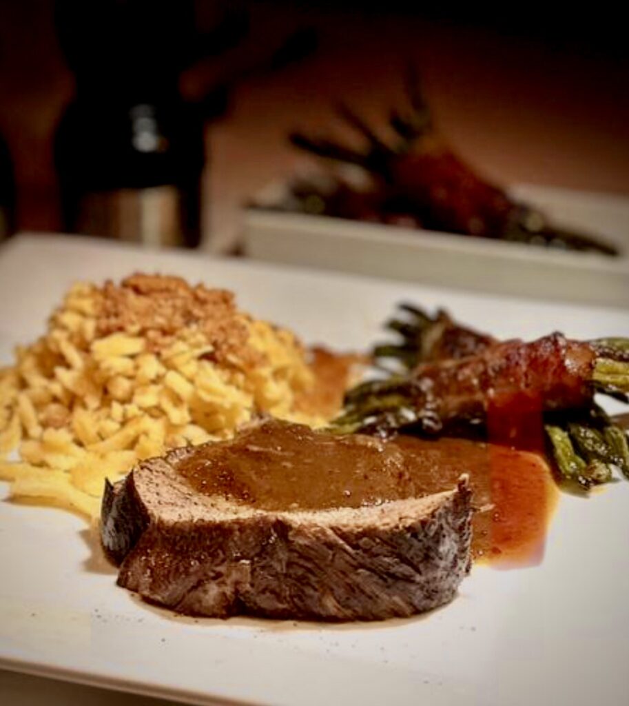 Geschmorte Lammkeule mit Spätzle und gerösteten Semmelbösel mit einer kräftigen dunklen Soße und Bohnen in Speck angerichtet.