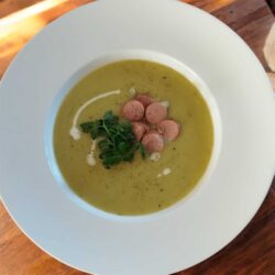 Cremige Kartoffel-Lauch-Suppe mit Wienerle in einem weißen , tiefen Teller serviert. Dazu mit Petersile und einem Schuss Sahne.