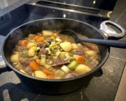 Frisch gekochter, dampfender Pichelsteiner Eintopf in einem Pfannen Harecker Kochtopf auf dem Herd, servierbereit mit einem Silikon Kochlöffel.