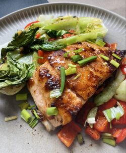 Teriyake-Lachs in der Pfanne gebraten, dazu Ofen-Pak Choi mit Paprika und Frühlingszwiebeln auf einem hellen Teller angerichtet.