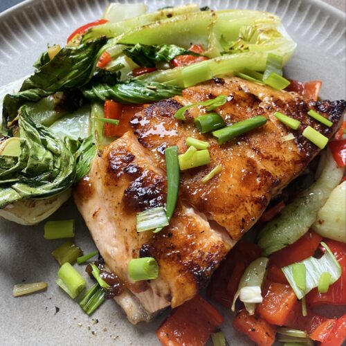 Teriyake-Lachs in der Pfanne gebraten, dazu Ofen-Pak Choi mit Paprika und Frühlingszwiebeln auf einem hellen Teller angerichtet.