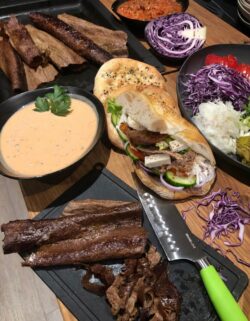 Nahaufnahme eines gedeckten Tisches mit einem Döner-Teller, Salat, verschiedenen Saucen, Fladenbrot und einer halbierten Rotkohlhälfte.