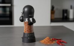 Hochwertige Gewürzmühle von der Kochblume, ideal für die Zubereitung von Speisen in einer Harecker Pfanne. Hier eine Gewürzmühle abgebildet mit einem und gemahlenen und selbst gemachten Döner Gewürz auf einer schwarzen Arbeitsfläche mit ein paar Chili´s daneben.