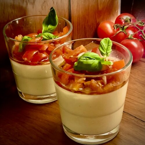 Servierfertige herzhafte Parmesan Panna Cotta mit fruchtigem Tomaten-Topping und frischen Kräutern als appetitanregender Gruß aus der Küche.