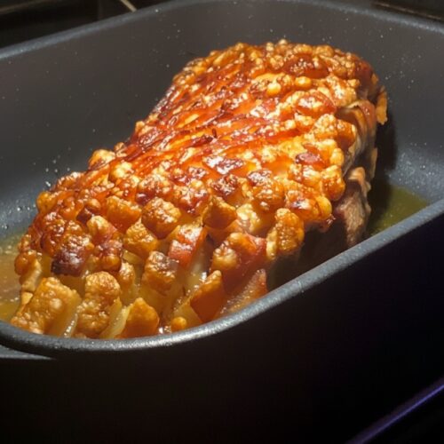 Frisch zubereiteter Schweinebraten mit goldbraun gebackener, knuspriger Kruste in einem dunklen Bräter im Backofen.